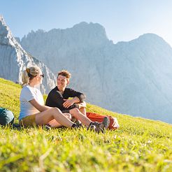 Junges Paar sitzt auf Wiese und blickt sich lächelnd in die Augen