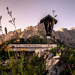 Rastbank und Gipfelkreuz mit imposanten Felsformationen des Wilden Kaisers im Hintergrund
