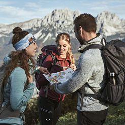 Drei Freunde stehen am Berg und blicken auf Faltkarte