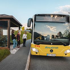 Gelber Bus hält vor einer Haltestelle mit wartenden Menschen