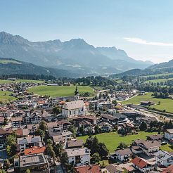 Blick auf Dorf mit Kirche und Gebirge im Hintergrund aus Vogelperspektive