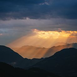 Orange Lichtstrahlen fallen durch Wolken auf Berglandschaft