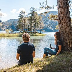 Zwei Frauen sitzen am Ufer eines Sees und unterhalten sich