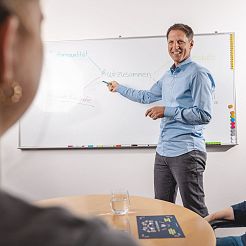 Mann steht im Besprechungsraum und zeigt auf Tafel