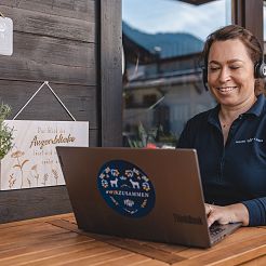 Frau sitzt auf Balkon bei einer digitalen Besprechung am Laptop