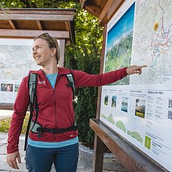 Frau in Wanderkleidung steht vor Karte und zeigt mit Finger auf Tour