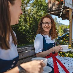 Zwei Frauen im Dirndl sitzen auf Bank und trinken Kaffee