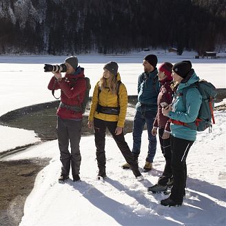 4-personen-sehen-einem-fotografen-am-verschneiten-seeufer-beim-fotografieren-zu-3